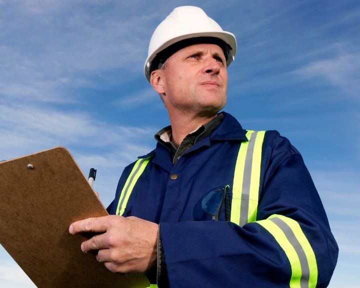 A roof inspector wearing a hard hat and holding a clipboard.